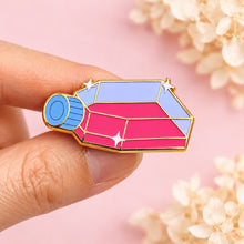 Hand holding a colorful cell culture flask enamel pin against a blush-pink background with ivory dried flowers.